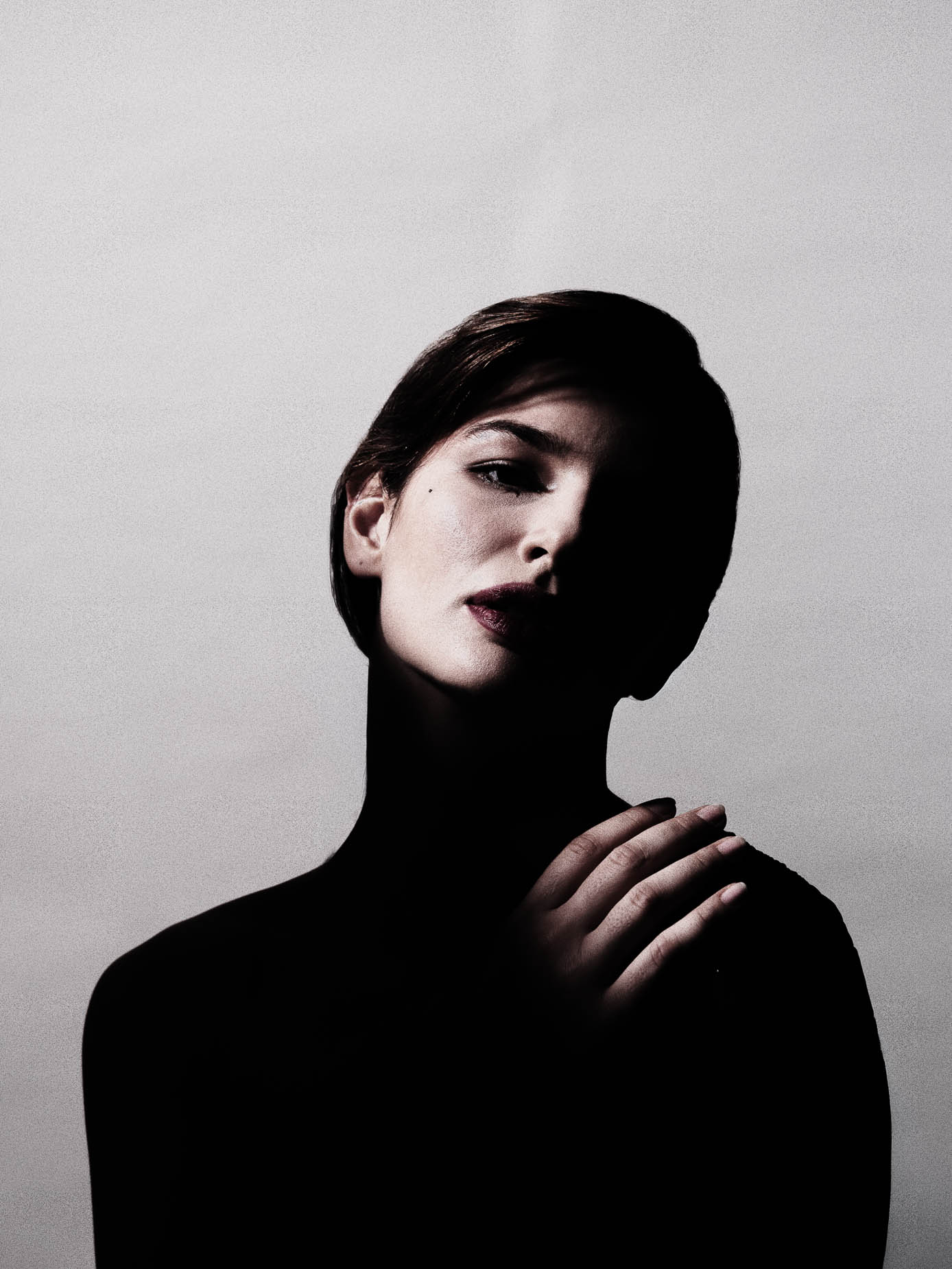 Low-key beauty studio portrait, face lit against a dark background with a steady, direct gaze
