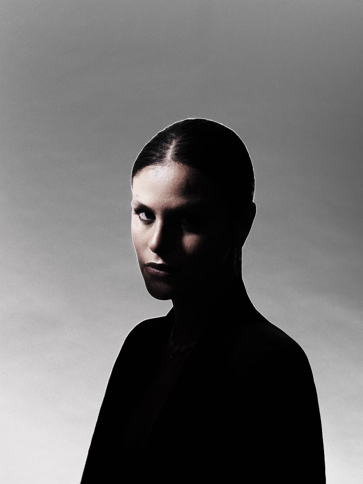 Low-key beauty studio portrait, dramatic side lighting carving the face out of a dark background