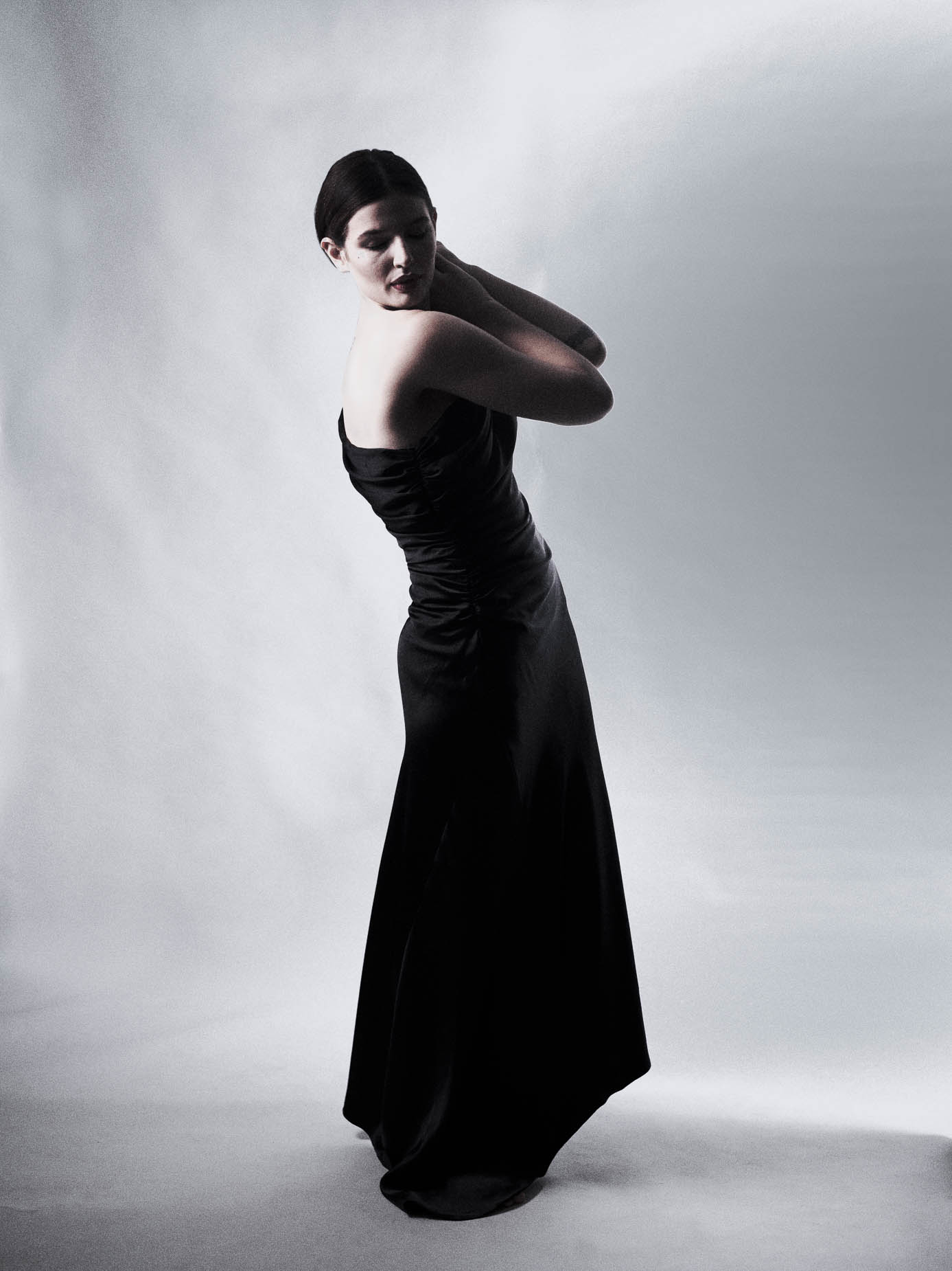 Woman standing full length in a black gown, one hand raised, softly lit studio backdrop