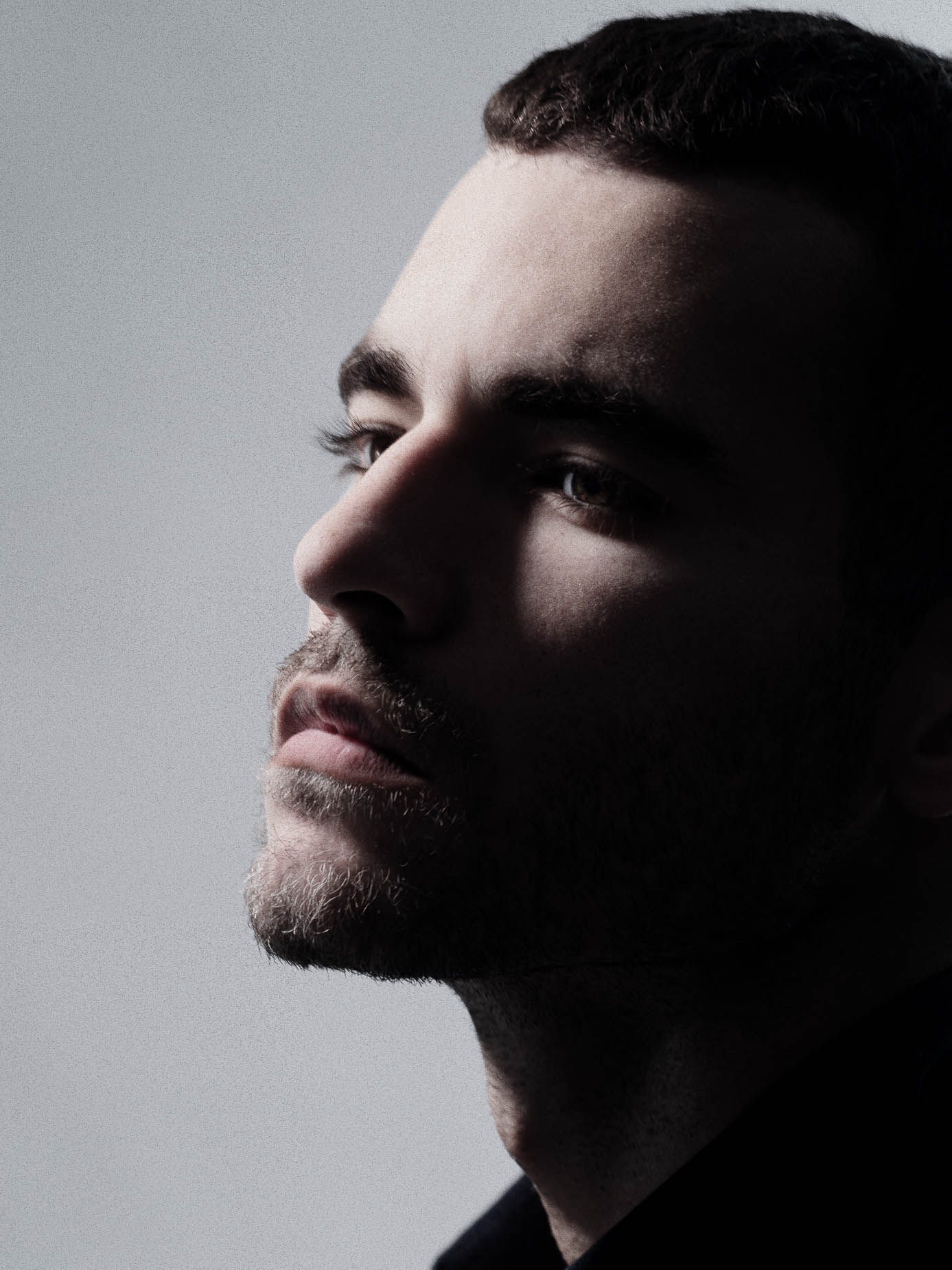 Man in close profile, dramatic side lighting splitting the face between light and shadow, dark background