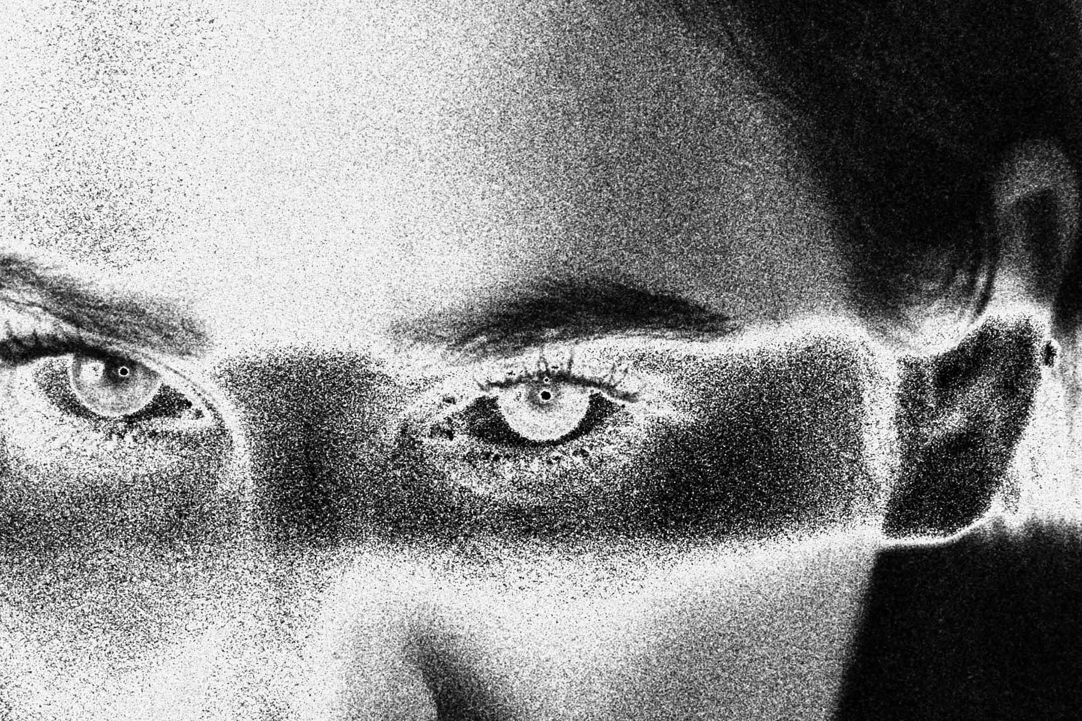 Extreme grainy close-up of a person's eyes staring directly at the camera, heavy film grain dissolving the skin into texture, dark hair visible at the edge