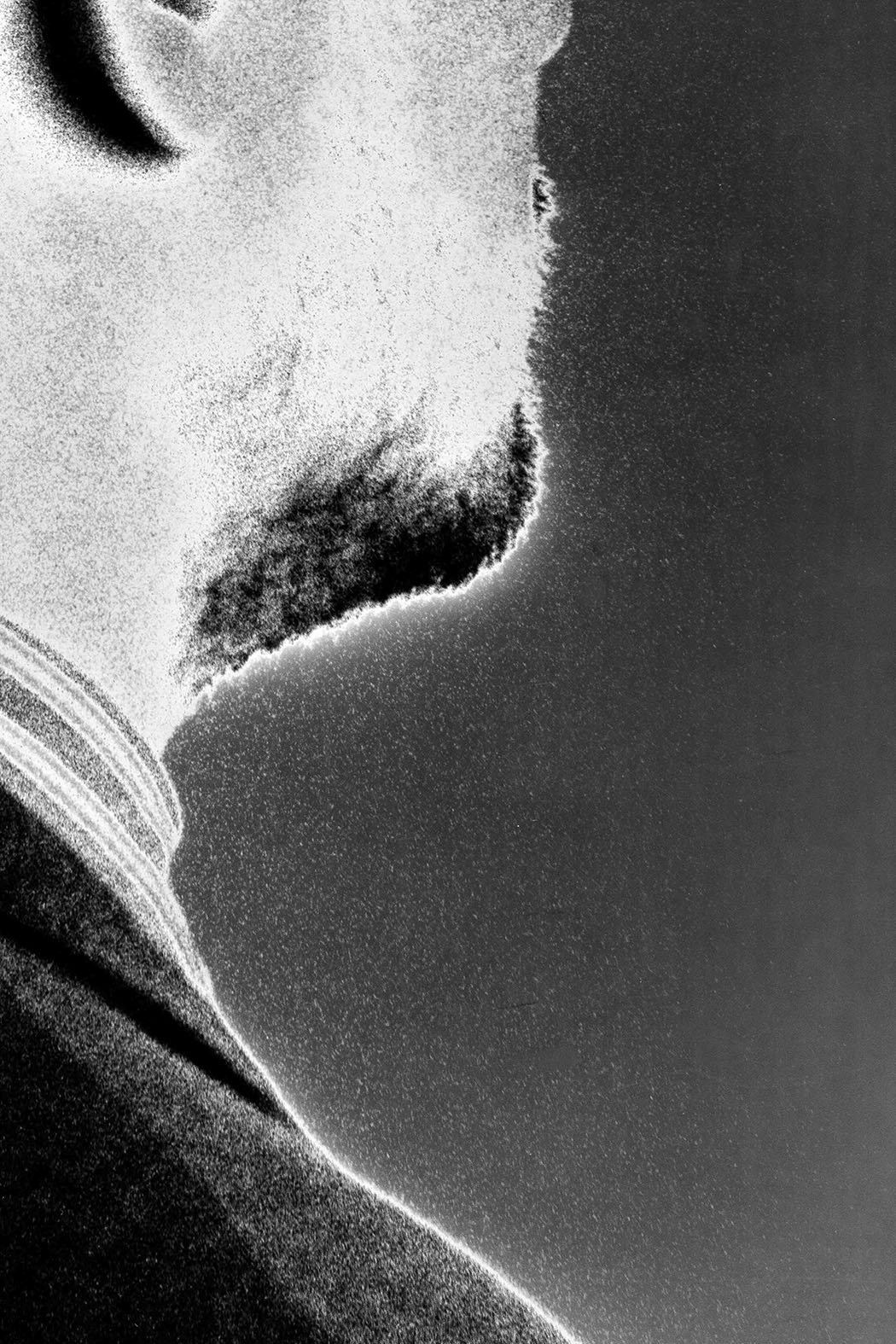 Extreme grainy close-up of a jaw and neck in profile, heavy black and white film grain, strong contrast between a lit cheek and a dark shadowed background