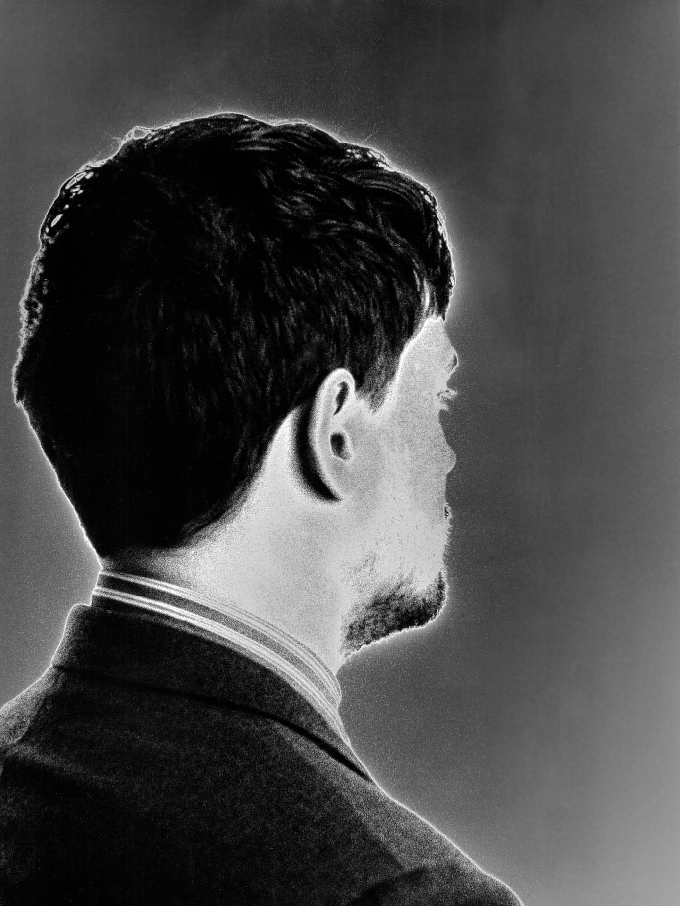 A bearded man's profile rendered as a vertical motion blur, jacket collar in sharp focus below the dissolving features