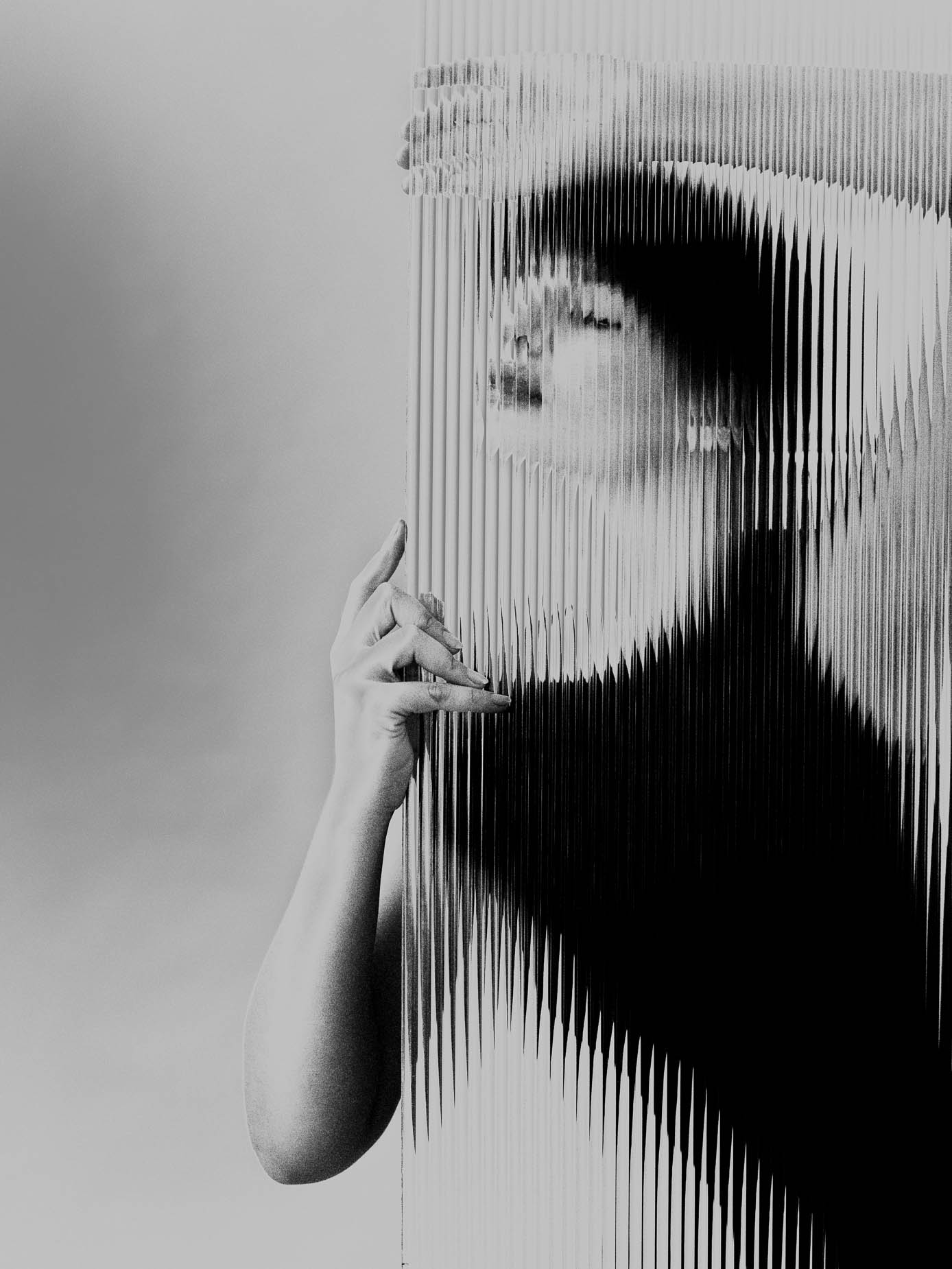 A narrow sliver of a face glimpsed through fluted glass, one hand gripping the edge of the glass panel, the rest of the body dissolving into striped bands