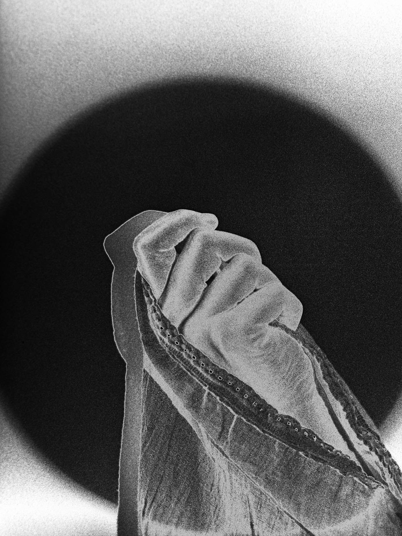 A hand and forearm emerge from a solid black circle, fingers curled, heavy film grain throughout the plain background