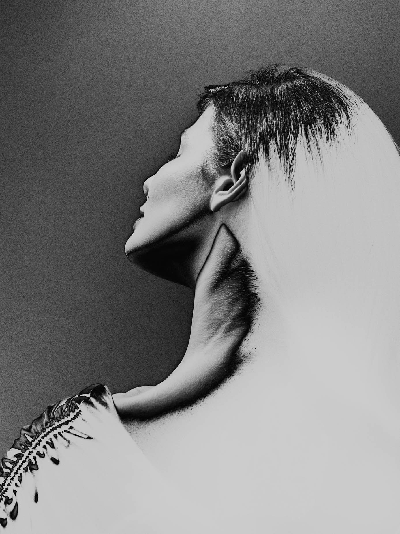 A profile portrait with head tilted back, hair swept off the face, neck and jaw lit against a dark background