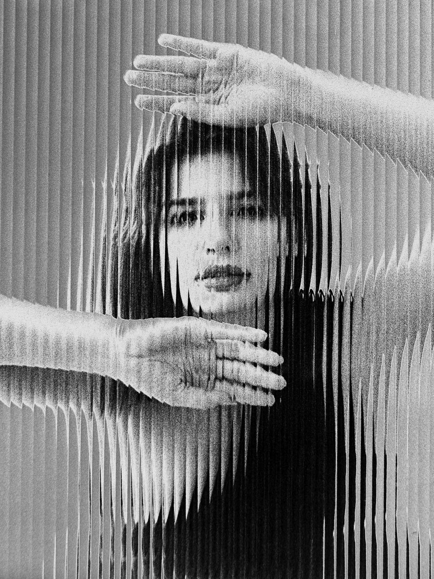 A face behind fluted glass framed by a raised hand above and a second hand pressed flat at the chest, the features breaking into vertical striped bands