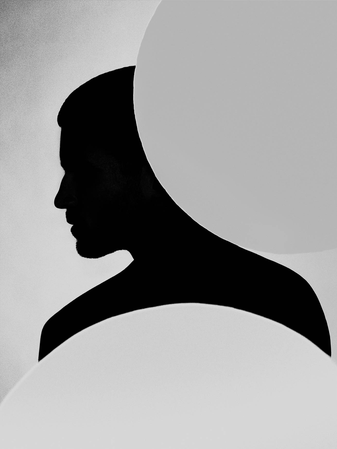 A bearded profile silhouette, the head partly eclipsed by a large pale circle against a plain background