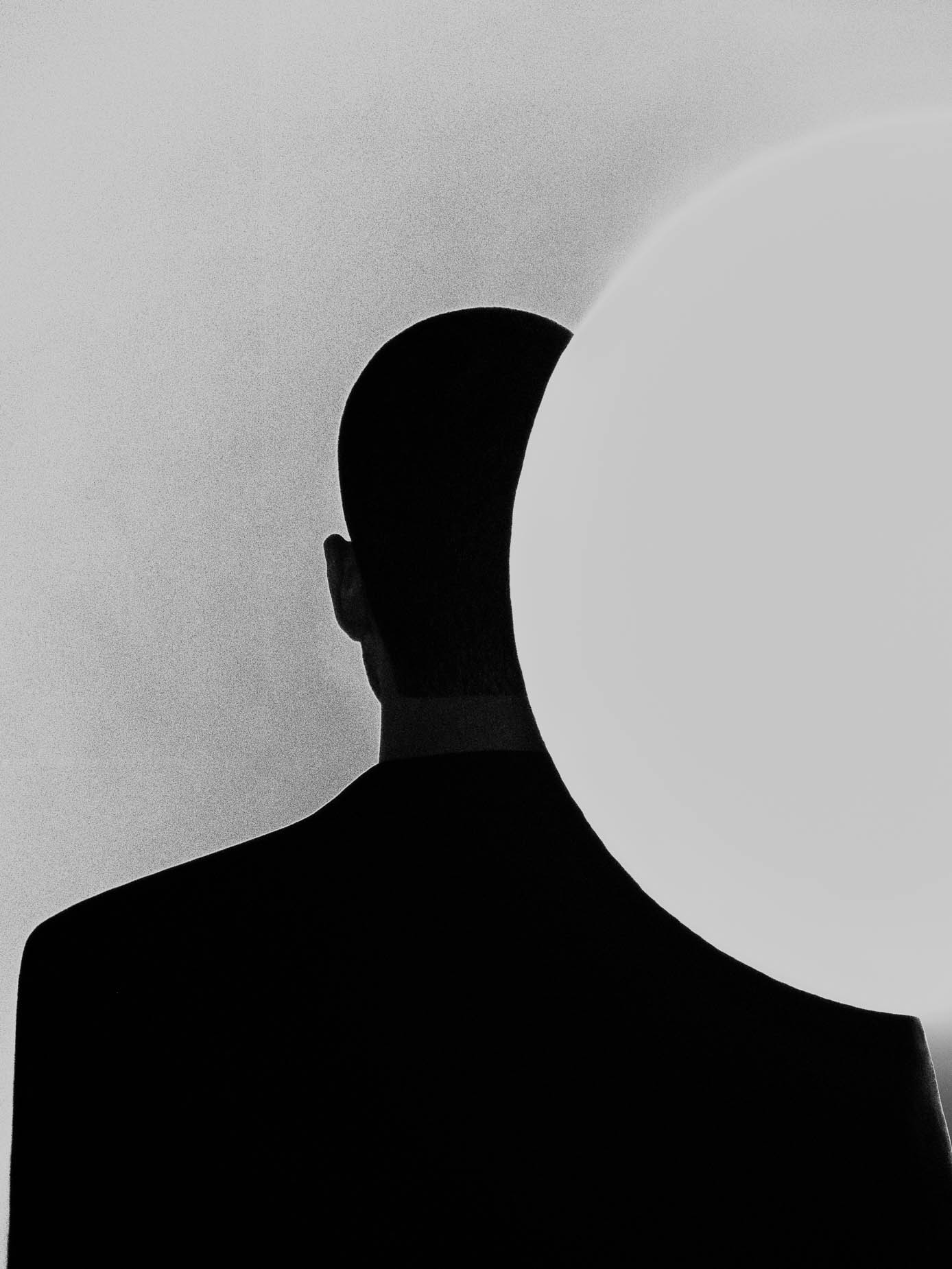 A silhouetted head and shoulders in profile, partly eclipsed by a large pale circle of light against a plain background