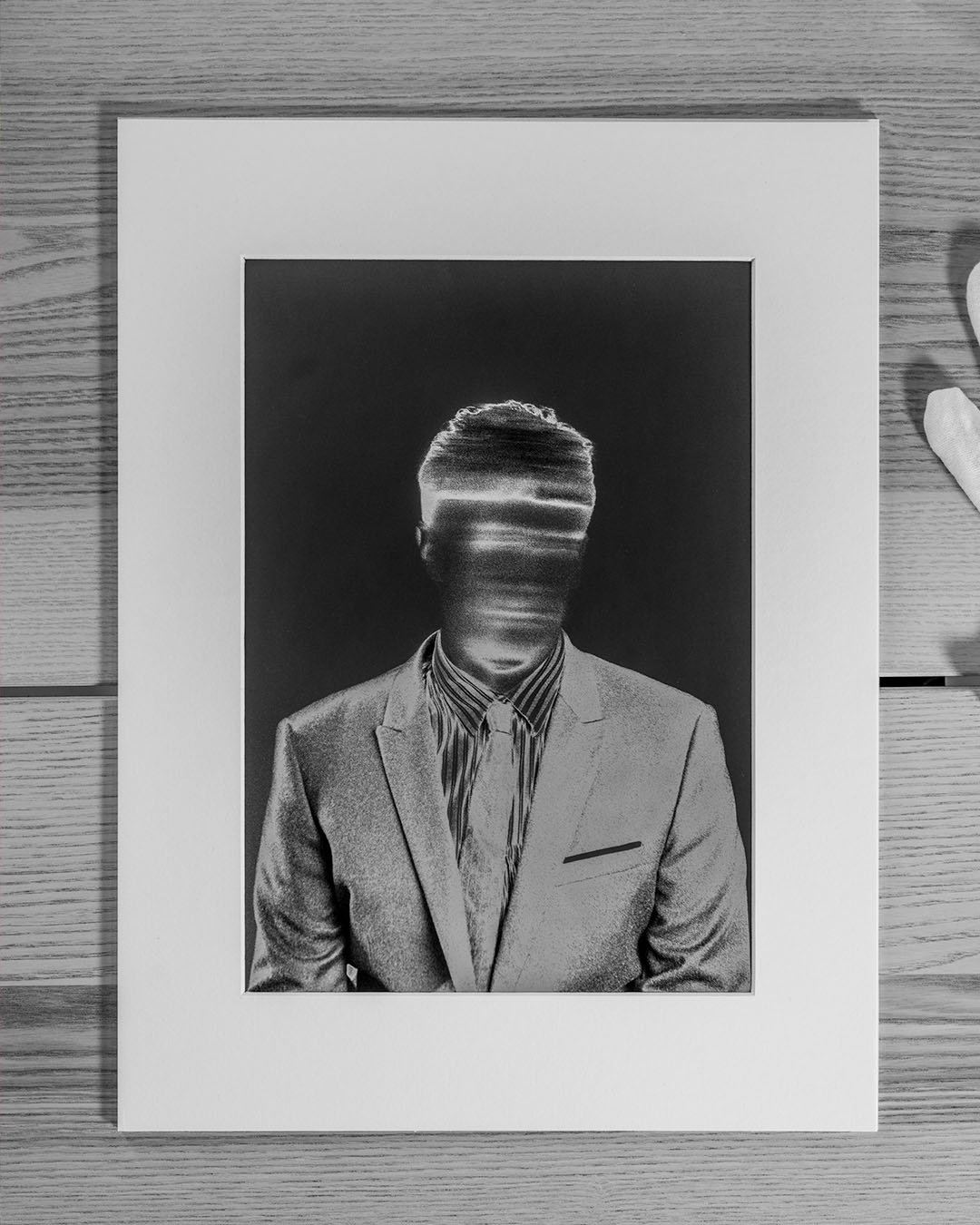 A matted black and white print lying on a wood floor, showing a man in a suit and striped tie whose face is blurred into pale streaks of motion, features unrecognizable