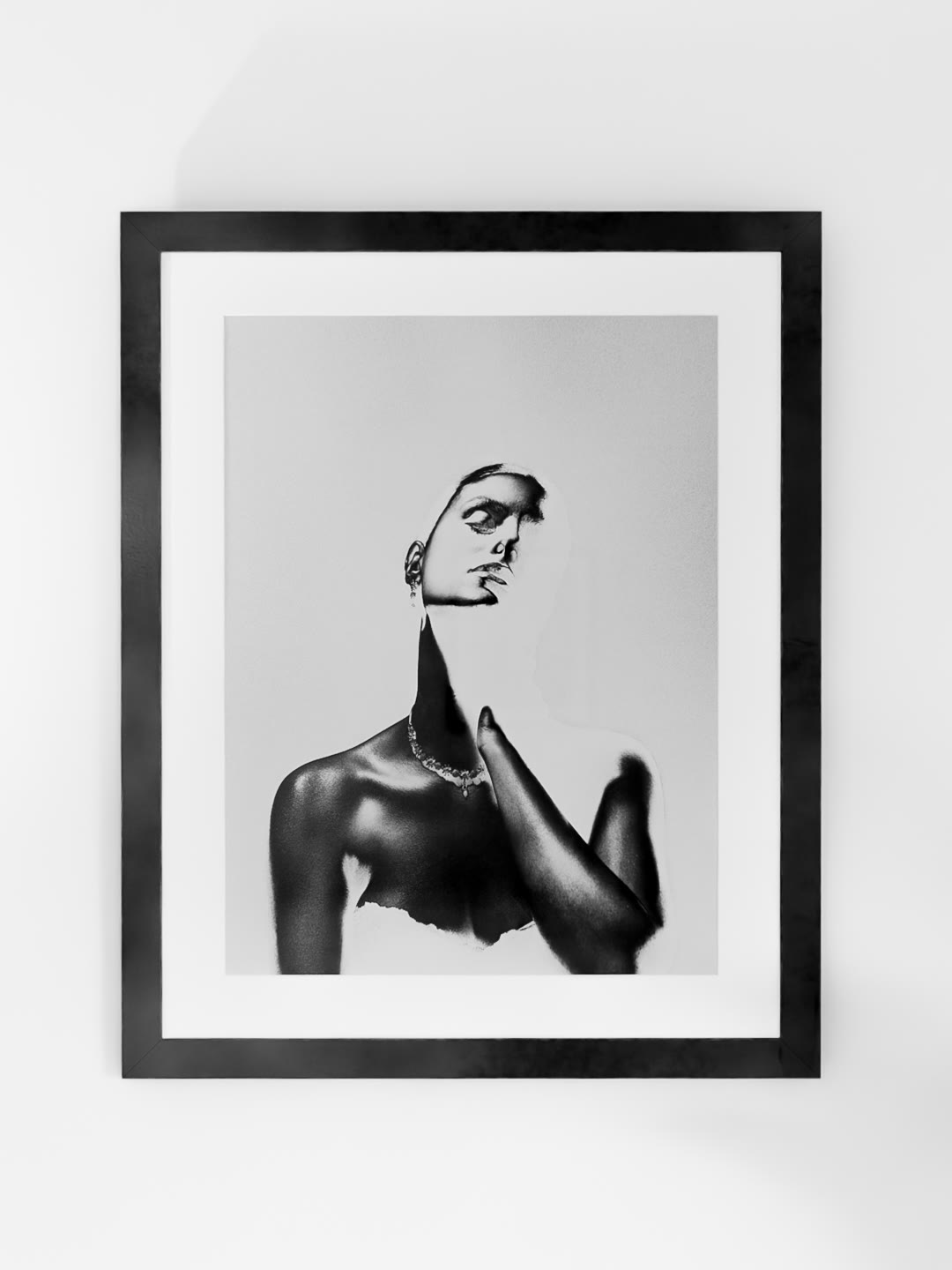 Persona from Mackie Lines, framed with a white mat on a white wall: a woman's face in light above a dark, metallic shoulder and chest, one hand raised to the throat